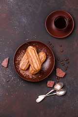 Chocolate eclair and coffee cup on dark background