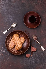 Chocolate eclair and coffee cup on dark background