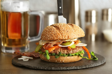 Slate plate with tasty bacon burger on table