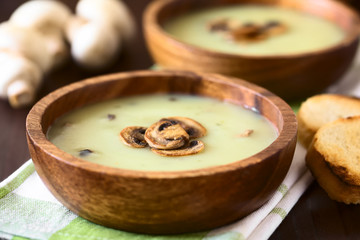 Mushroom cream soup garnished with roasted mushroom slices served in wooden bowls, photographed...