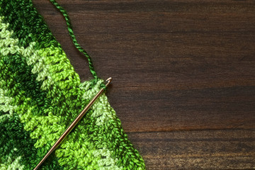 Crochet handicraft, making a place mat out of green yarn with a pattern of double stitches using a metal crochet hook or needle, photographed overhead with natural light