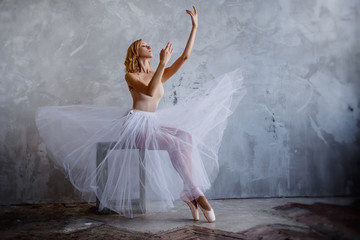 Young and slim ballet dancer is posing in a stylish studio with big windows