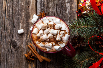 Cup of hot cocoa on wooden background with fir tree and snow effect. Traditional beverage for winter time