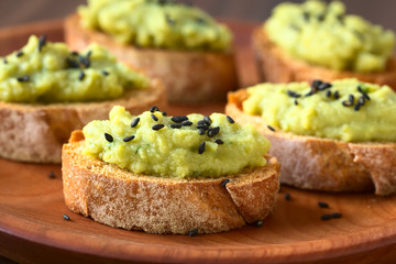 Bread slices with green pea and parsley spread garnished with black sesame seeds, photographed with natural light (Selective Focus on front of the spread on first bread)