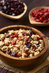 Crunchy oatmeal cereal with almond and dried goji berries and cranberries in wooden bowl, photographed with natural light (Selective Focus, Focus in the middle of the bowl)
