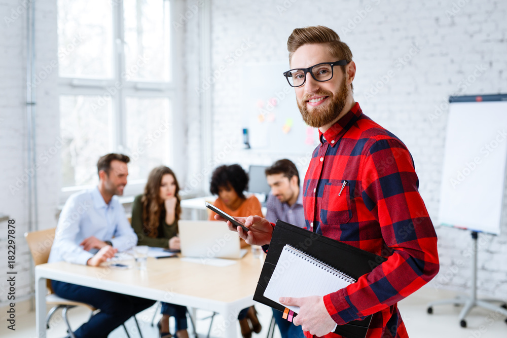 Wall mural Portrait of happy student standing at university classroom with colleagues in background