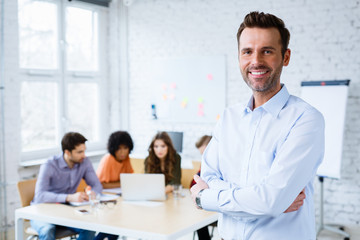Portrait of happy teacher standing in classroom with students in background