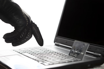 Hackers gloved hand at work on a laptop with stolen credit card