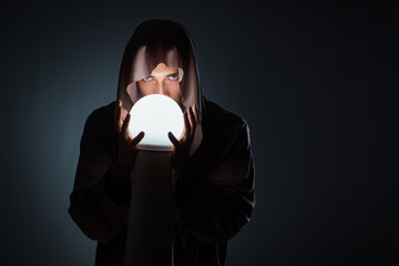 Young wizard with crystal ball in dark room