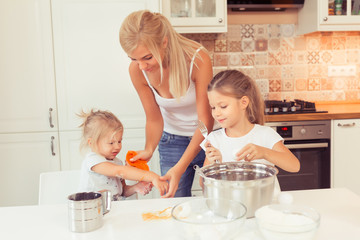 Cooking healthy food at home in the white kitchen. Happy family in the kitchen. Mother and children daughters are preparing the apple cake