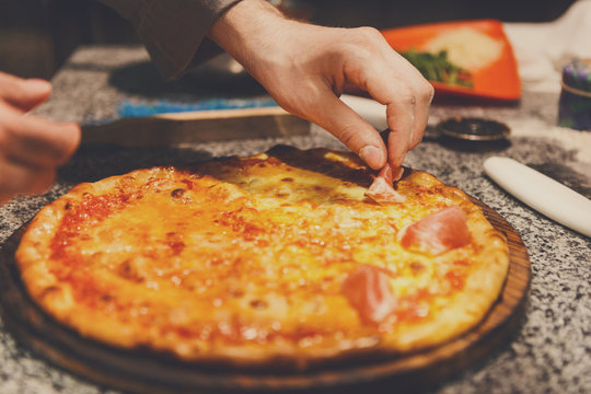Adding prosciutto to pizza, close up