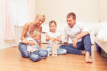 Cheerful family spending time together at home,. Daddy, mommy and little daughters lying on the wooden floor and playing with a wooden tower game.