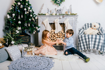Children playing in new year interior room. Crhistmas tree with balls. Winter holidays mood. Happy kids enjoying toys. Young friends sitting and joking. Boy and girl together. Celebrating feast.