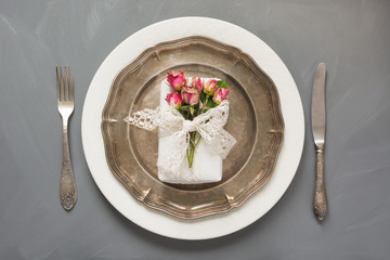 Festive table setting, female gift with flowers, vintage dishware, silverware and decorations on gray. Top view.