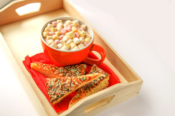 Cocoa drink with marshmallows and pieces of sweet homemade cake in a wooden tray