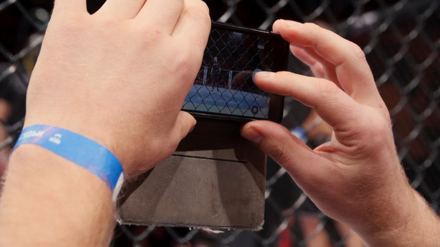 Man shooting MMA, mix fight or cage fighting on video using phone close up. Male hand shooting sporting event on smartphone. Man shooting photos in a crowd on his mobile phone
