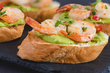 Bruschetta italian snack sandwiches with avocado cream and prawns decorated by parsley and chilli peppers.