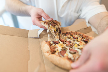 Men's hands take a piece of hot pizza. The man will eat delicious pizza with cheese. Focus on pizza.
