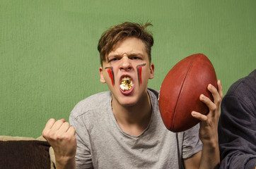 Hyped kid with mouth full of popcorn holding american football ball, Superbowl concept 