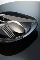 Empty plate with knife and fork, spoon, on a black background