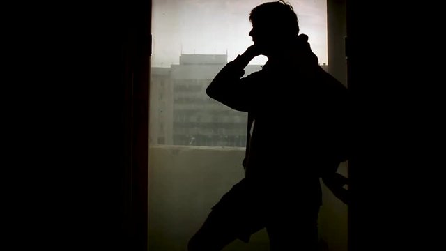 Silhouette of dander in front of window. Footage. Shadow of professional man pole dancer on pylon near window.