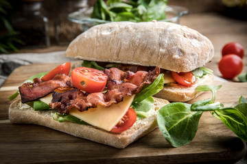 Ciabatta sandwich with arugula salad, bacon and yellow cheese.