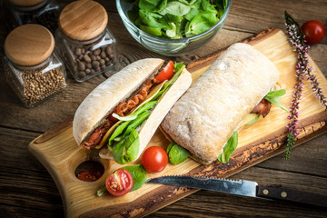 Ciabatta sandwich with arugula salad, bacon and yellow cheese.