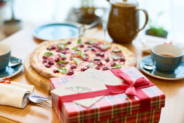 Close up view of pretty decorated gift box tied with ribbon and card attached to it standing on dinner table, holiday background