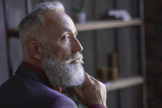 Close up face of side view serene unshaven old businessman thinking while situating in modern apartment. Pensiveness concept. Copy space