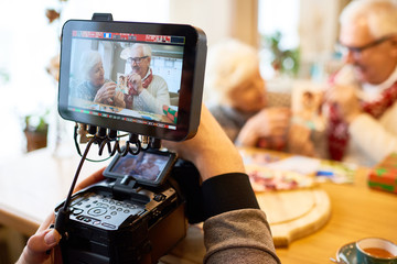 Unrecognizable man recording video of senior couple showing family photos, focus on modern 4k vide...