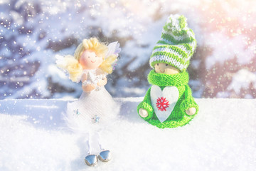 Toy wooden girl in Scandinavian style in knitted green clothes on the snow and angel. Christmas toys.