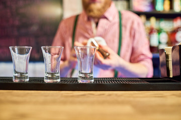 Mid section of unrecognizable bartender cleaning glasses at bar counter row of little empty shots in row in foreground
