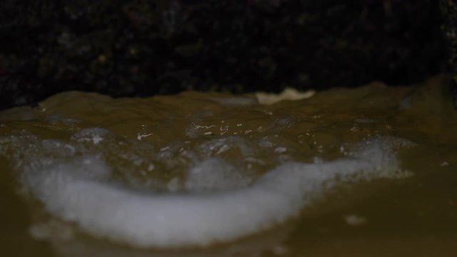 A close-up shot of a rusted hole in a shipwreck as the tide ebbs in and out.