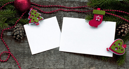 Christmas card with clean sheets the attached decorative clothespegs to fir-tree branches and white paper on a wooden background. 