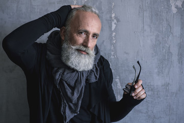 Portrait of serene bearded fashion old man keeping glasses. Copy space. Glamour concept