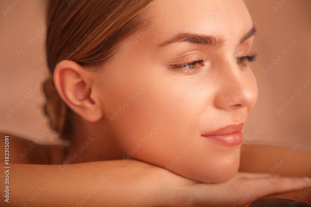 Wall mural Close up of face of sensual girl lying and relaxing. She is leaning head on arms and smiling. Peace and comfort concept