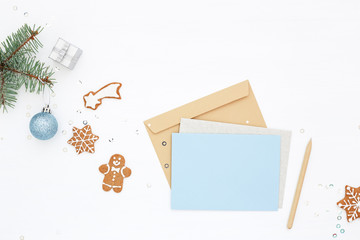Christmas workplace with blue blank card, envelope, gingerbread man, gift and New Year decoration on white. Winter holidays, Sending Congratulations. Top view