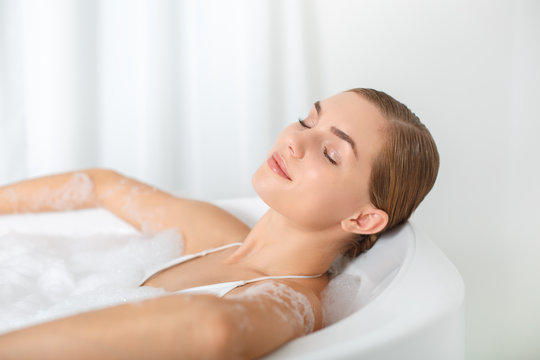 Calm young woman is lying in bathtub and relaxing. Her eyes are closed with pleasure