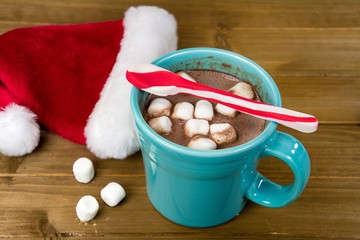peppermint striped spoon on hot chocolate drink with marshmallow and Santa cap on rustic wood
