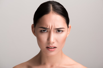 Full of rage. Close-up portrait of young angry asian woman is looking at camera with annoyance while frowning her forehead. Isolated background