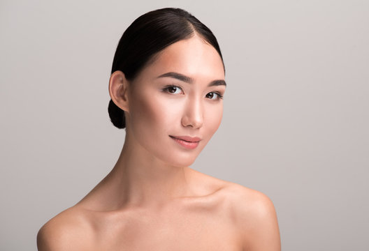 Seducing glance. Portrait of charming naked positive young asian woman is looking at camera with slight smile. She is demonstrating perfect and fresh skin. Isolated background
