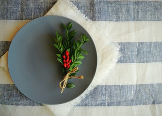 Dark blue plate, nandmade white linen no sew napkin on striped white blue linen tablecloth. Top view.