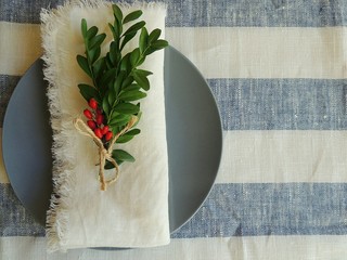 Dark blue plate, nandmade white linen no sew napkin on striped white blue linen tablecloth. Top view.