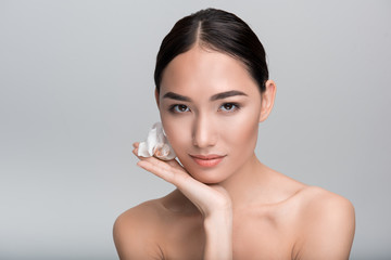 Keep my skin soft. Portrait of sweet enchanting young naked asian woman is looking at camera thoughtfully while leaning on palm with flower. Isolated background with copy space. Skincare concept