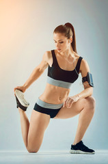 Fototapeta na wymiar Healthy and strong. Attractive young sporty brunette wearing a two piece sport clothing leaning on one leg while doing a stretching exercise and bending her knee.