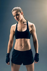 Fototapeta na wymiar What are you waiting for. Muscular young sportswoman wearing boxing wraps showing her well trained body while posing for the camera over a dark background.