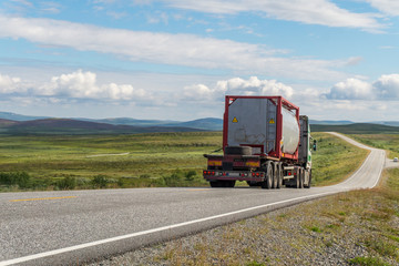 Large tanker truck on the road on a background of a green meadow and clouds