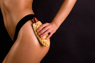 Mid section of sporty slim woman holding hot-dog, anti-cellulite concept, fast food isolated on black background