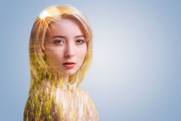 Tender look. Pensive blonde girl standing against the light background and looking into the camera enigmatically while posing.