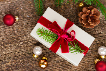 Christmas gift- evergreen fir tree twigs and christmas paper gift on wooden aged background with small decorations, flat lay top view